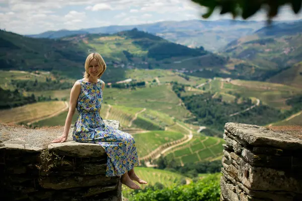 stock image A woman in a light dress sits on a stone wall of the vineyards in the Douro Valley.