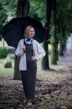 Parkta şemsiyesi olan bir kadın duruyor..