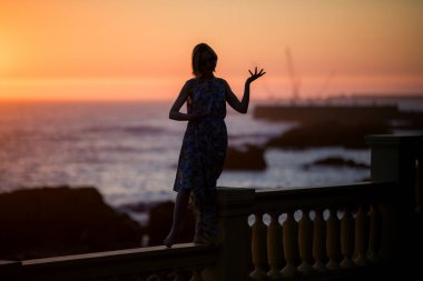 Portekiz 'de okyanus kıyısındaki bir güvertede gün batımına karşı siluet yaratan bir kadın..