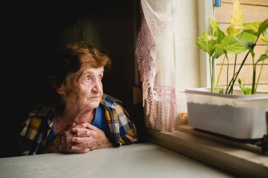 Evindeki bir masada oturan bir büyükanne, pencereden dışarı bakıyor..