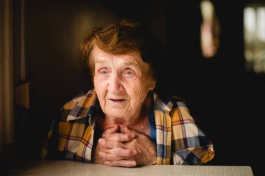 Yaşlı bir kadın masada otururken duygusal konuşuyor, dokunaklı bir portre..