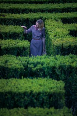 Eski bir Avrupa parkındaki labirentte uzun yeşil çalıların arasında bir kadın duruyor..