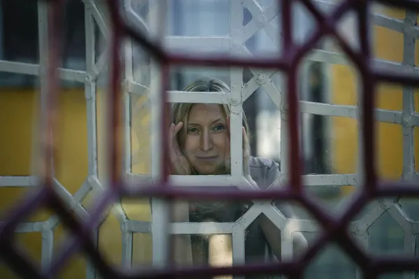 stock image A woman gazes through a window with antique grilles in an old estate.