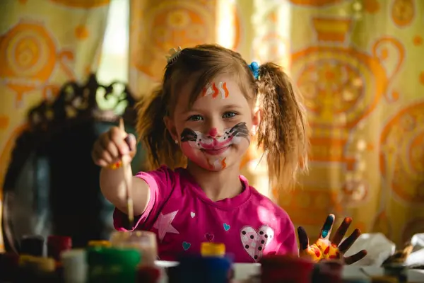 stock image A cute girl with a painted face painting with brushes.