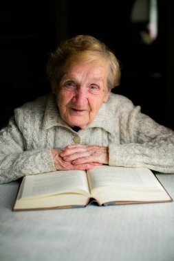 Yaşlı bir kadın, sayfaları çevirirken sakin ve odaklanmış bir şekilde düşünceli bir portreye yakalanmış bir kitap okur..