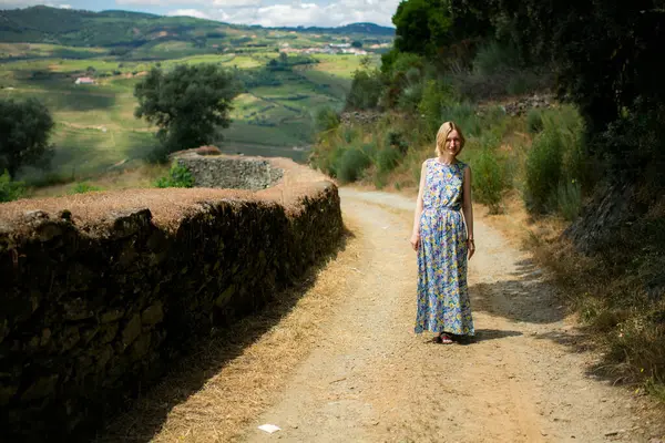 stock image A full-length portrait of a woman standing on a path leading to the vineyard, surrounded by the lush green landscape of the Douro Valley.