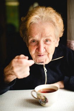 Yaşlı bir kadın rahat rahat evinde oturur, sıcak bir fincan çayın tadını çıkarır.. 