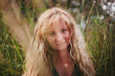 Saman renkli saçlı bir kadının portresi, bir tarlada duruyor, altın güneş ışığıyla yıkanmış, yüzü sıcacık ve doğal güzellikle parlıyor..