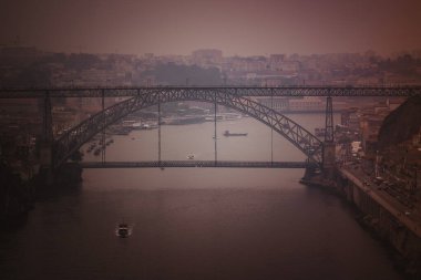 The Douro River and Dom Luis I Bridge enveloped in dense smoke from nearby wildfires, illuminated by the soft orange glow of the setting sun filtering through the haze. clipart