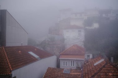 Houses and rooftops in Porto blanketed in thick morning fog, with only the faintest outlines visible through the mist. clipart