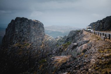 Serra da Estrela dağlarının arasından geçen bir yol bulutlu gökyüzünün altında dramatik bir atmosfer yaratıyor..