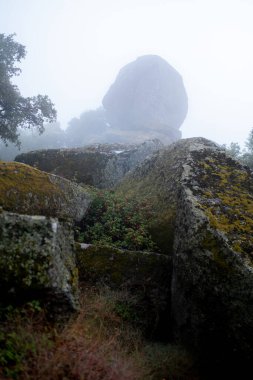 Massive boulders stand tall as fog descends into the valley in Monsanto, Portugal, creating a mystical and moody scene. clipart