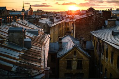 Günbatımında Saint Petersburg çatılarının manzarası, sıcak, altın ışıkla yıkanmış, şehrin ufuk çizgisinin romantik cazibesini yakalıyor..