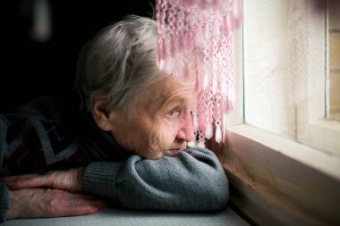 Yaşlı bir kadın ne yazık ki evinin penceresinden dışarı bakar, gözleri derin bir melankoli hissini yansıtır..