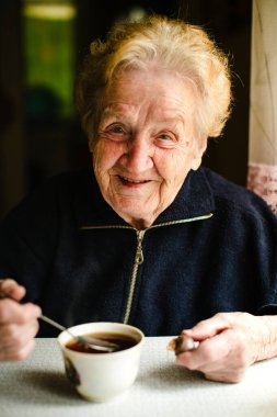 Neşeli yaşlı bir kadın bir fincan çayın tadını çıkarıyor, sıcak gülüşü bu samimi portrede pozitiflik saçıyor.