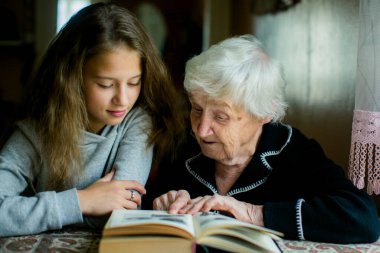 Nazik, gümüş saçlı bir büyükanne, genç torunuyla birlikte hassas bir anı paylaşan bir kitap okur..