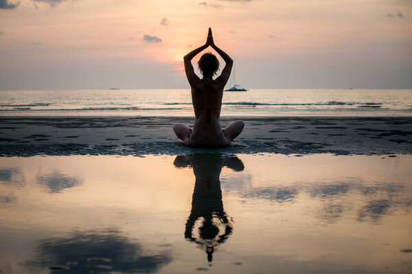 Силуэт женщины-йоги, практикующей на пляже с ее отражением в воде.