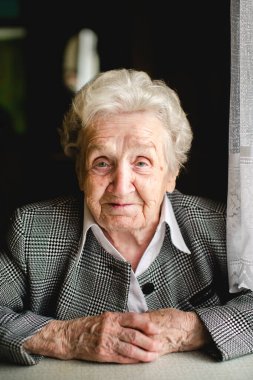 İş elbisesi giymiş yaşlı bir kadının portresi. Kırışık elleri nazikçe dinleniyor. Sıcaklık ve asalet saçıyor..