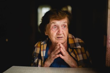 Derin bir duygusal ifadeye sahip yaşlı bir kadının portresi, elleri nazikçe sımsıkı sarılmış, sessiz bir güç ve hassasiyet anını yakalıyor..