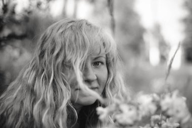 Tarlada dikilen bir kadının siyah-beyaz portresi, açık renk saçları rüzgarla hafifçe hareket ediyor. Görüntü, doğal zarafetle dolu sessiz ve içe dönük bir anı yakalar..