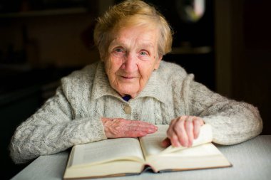 Kalın bir kitap okuyan bilge yaşlı bir kadının portresi. Yüzü sakin ve odaklanmış. Bilgi, sabır ve öğrenmenin sessiz keyfi yayılır..