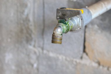 Kapalı, paslı ve kirli çelik su musluğu. Yeşil yosun kaplı eski su tabakası.