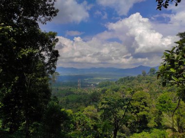 Yemyeşil ormanları, dağları ve güzel bulutlarla çerçevelenmiş bir köyü olan bir tepeden panoramik manzara. Doğa, manzara ve doğa ile ilgili içerik için mükemmel..