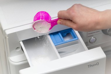 Lviv, Ukraine - December 20, 2024: hand pouring detergent into LG ThinQ washing and drying machine clipart