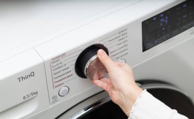 Lviv, Ukraine - December 20, 2024: hand turning on LG ThinQ washing and drying machine clipart