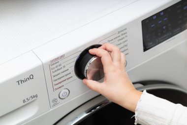 Lviv, Ukraine - December 20, 2024: hand turning on LG ThinQ washing and drying machine clipart