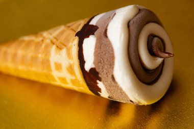 Çikolatalı dondurma külahı ve altın arka planda Vanilya Girdabı