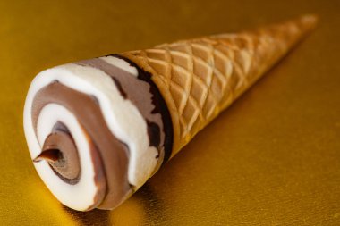 Çikolatalı dondurma külahı ve altın arka planda Vanilya Girdabı