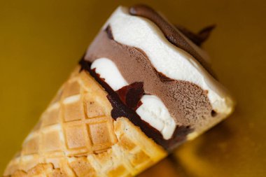 Çikolatalı dondurma külahı ve altın arka planda Vanilya Girdabı