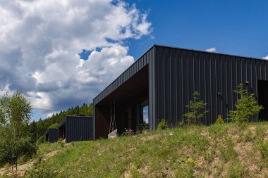 Karpatlar 'daki çimenli bir tepenin üzerinde bulunan ahşap ve metal cepheli modern kamaralar serisi. Güneş batıyor, binalara ve çevresindeki doğaya sıcak altın bir ışık saçıyor, arka planda yoğun bir orman görünüyor..