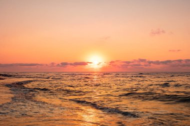 Turuncu gökyüzü ve dalgalarla denizin üzerinde dramatik bir gün batımı