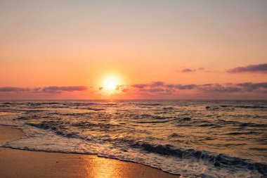 Turuncu gökyüzü ve dalgalarla denizin üzerinde dramatik bir gün batımı