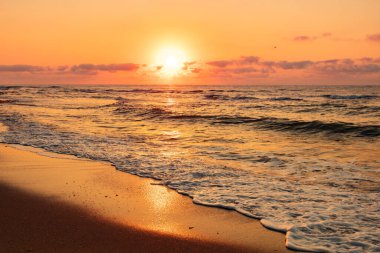 Turuncu gökyüzü ve dalgalarla denizin üzerinde dramatik bir gün batımı