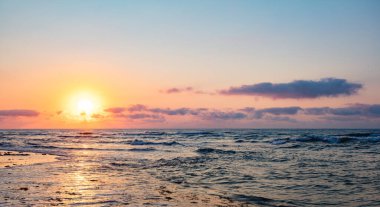 Turuncu gökyüzü ve dalgalarla denizin üzerinde dramatik bir gün batımı