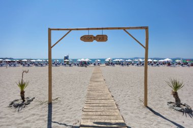 Tahta yolu ve Pomorie tabelası olan güneşli bir sahil.