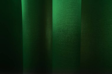 Parlak bir yüzeyi olan yeşil bir perdenin yakın çekimi yumuşak kıvrımlar oluşturur ve hafif bir ışık ve gölge eğilimi yaratır.
