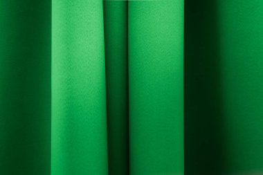 Parlak bir yüzeyi olan yeşil bir perdenin yakın çekimi yumuşak kıvrımlar oluşturur ve hafif bir ışık ve gölge eğilimi yaratır.