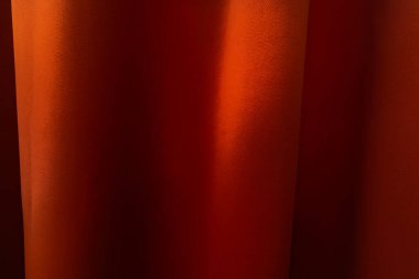 Parlak bir yüzeyi olan turuncu bir perdenin yakın çekimi yumuşak kıvrımlar oluşturur ve hafif bir ışık ve gölge eğilimi yaratır.