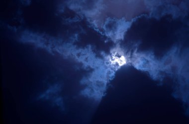 Bulutlu gece gökyüzü ve bulutlarda ay. Ay bulutların arasından parlıyor..