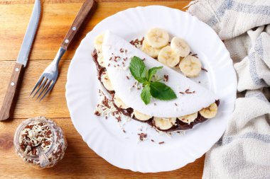 homemade tapioca or beiju stuffed with banana and chocolate on white plate over rustic wooden table. top view clipart