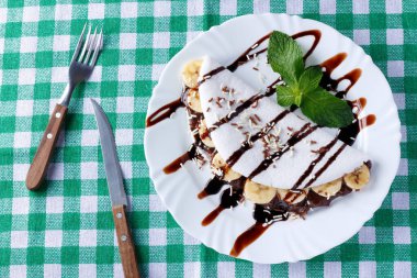 Ev yapımı tapyoka ya da muz ve çikolatayla doldurulmuş beyaz tabak üzerine sade ahşap masa. en üstteki görünüm