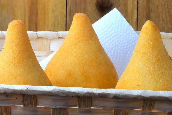 Coxinha in the basket, traditional Brazilian cuisine snacks stuffed with chicken, isolated on rustic wooden table. Close up