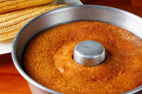 corn cake on in the pan baking form on rustic wooden table. Typical Brazilian party food. Selective focus