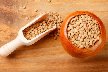 Köy ahşap masadaki ahşap kasede kahverengi çiğ mercimek. Üst görünüm