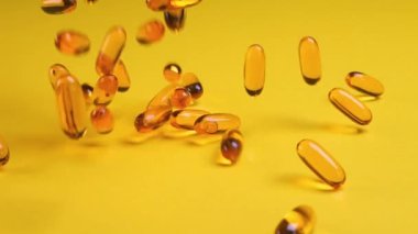 Omega balığı yağı besin takviyesi sarı arka plana düşüyor. Omega balığı yağı softgels beslenme takviyesi arka planı. Sağlıklı yaşam ve kalp sağlığı kavramı. Yavaş çekim