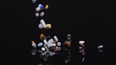 Siyah arka plana düşen farklı haplar. İlaçlar, haplar, antibiyotikler, vitaminler, sağlık hizmetleri, ilaç endüstrisi, uyuşturucu kullanımı, ilaç konsepti. Yavaş çekim